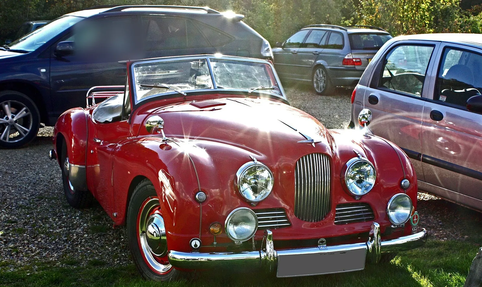 A red classic car parked on gravel